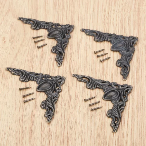 Quatre ornements d’angle couleur bronze à feuilles et volutes, accompagnés de douze clous sur un fond en bois