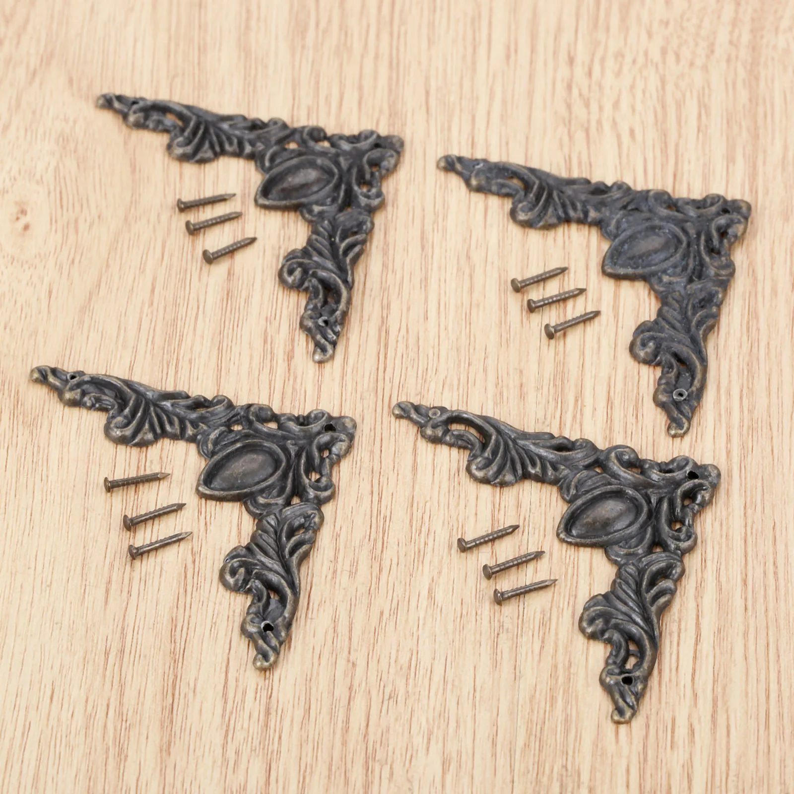 Quatre ornements d’angle couleur bronze à feuilles et volutes, accompagnés de douze clous sur un fond en bois