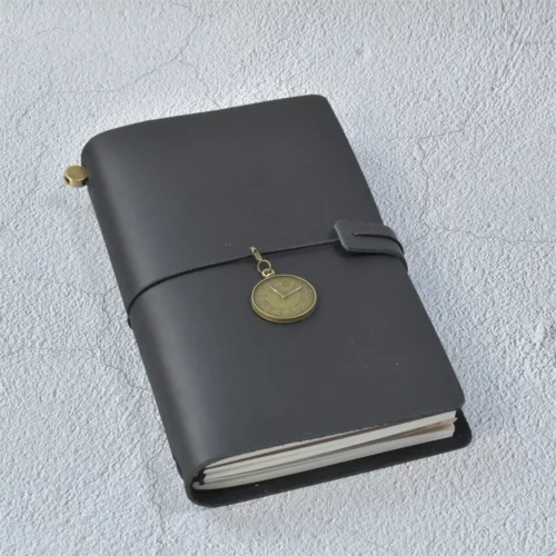 Carnet rechargeable noir au format A5, avec une breloque ronde couleur laiton ornée de chiffres romains